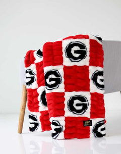 Red and white Georgia Hugs Minky Couture blanket folded and draped over a chair, showing its textured logo pattern.