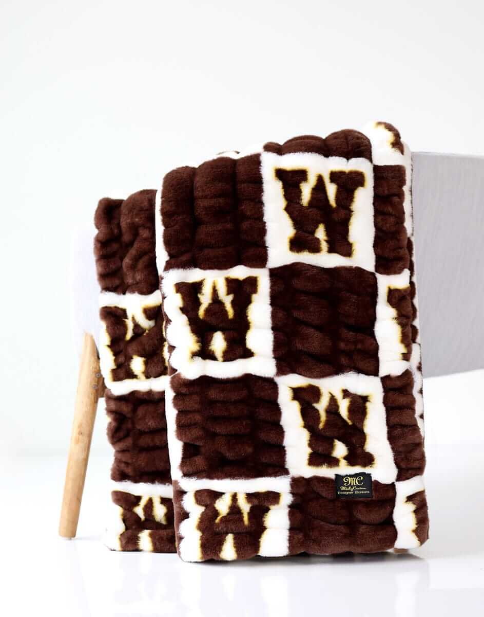 Wyoming Cowboys Hugs Minky Couture blanket folded over a chair, featuring brown and cream logo pattern.