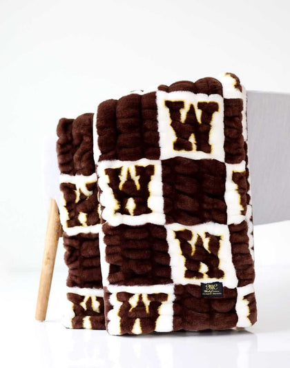 Wyoming Cowboys Hugs Minky Couture blanket folded over a chair, featuring brown and cream logo pattern.