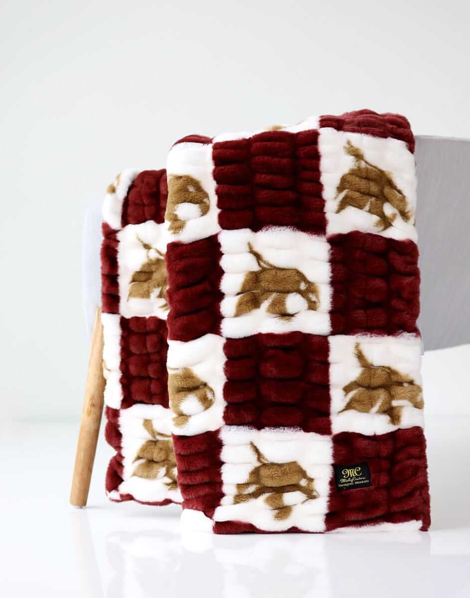 Texas Bobcats Hugs Minky Couture blanket folded and draped over a chair, showing maroon, white, and gold pattern.