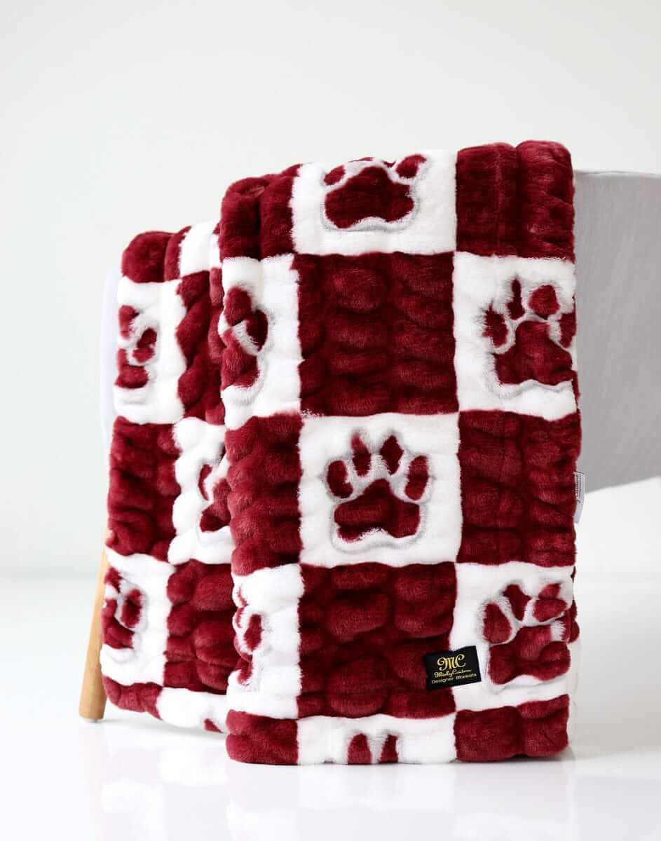 Mississippi State Hugs Minky Couture blanket folded over a chair, featuring maroon and white paw print pattern.