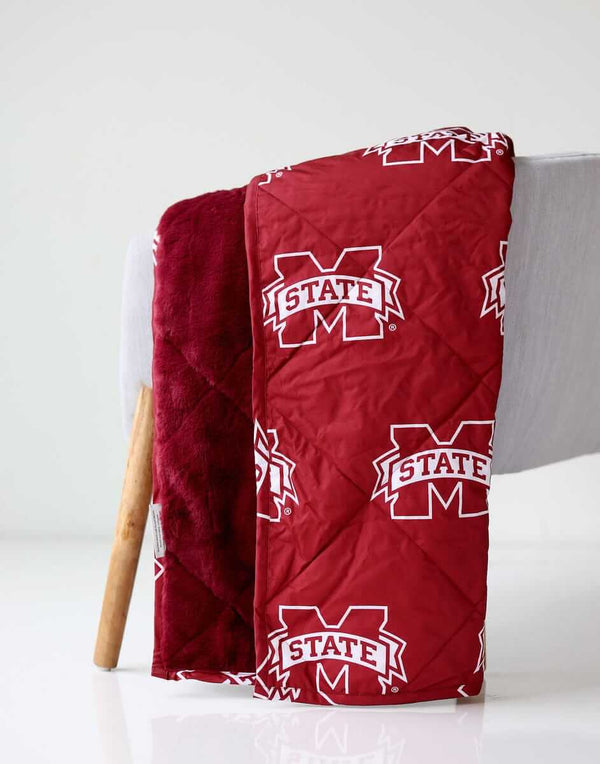 Mississippi State Everywhere Minky Couture blanket folded over a chair, showing maroon logo side and plush lining.