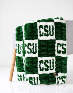 Colorado State Rams Minky Couture blanket folded over a chair, featuring green and white textured lettering pattern.