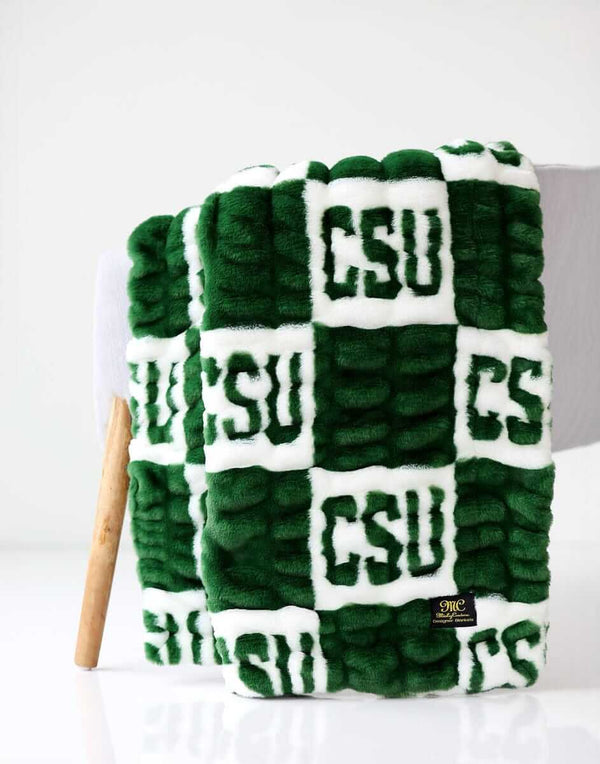 Colorado State Rams Minky Couture blanket folded over a chair, featuring green and white textured lettering pattern.