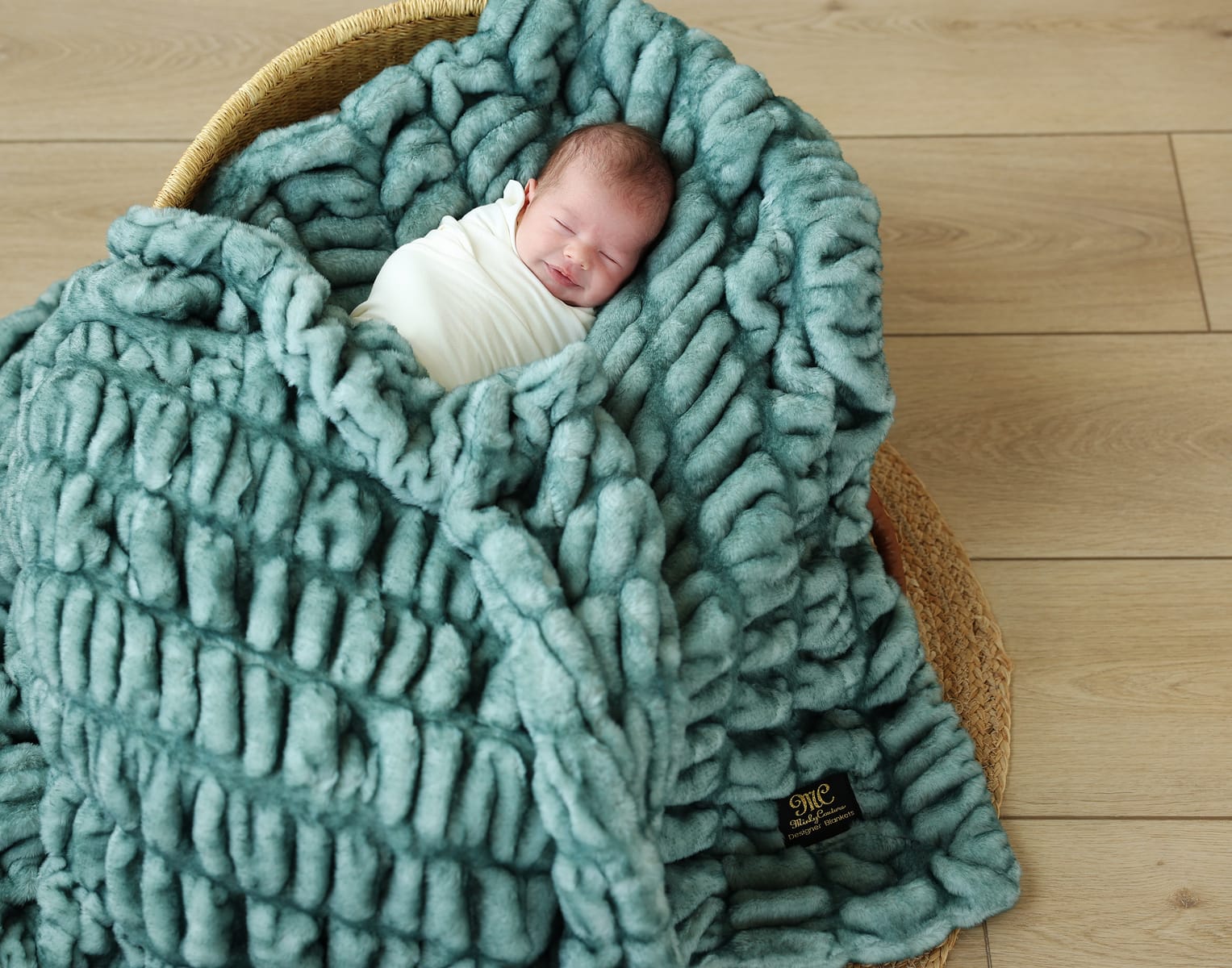 A peaceful baby swaddled in a Hugs Jade Blanket, showcasing its plush jade color and soft texture.