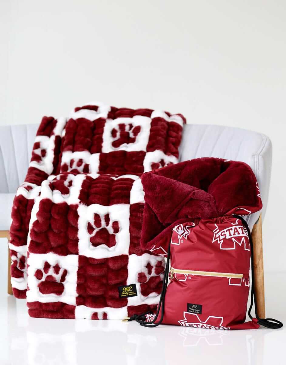 Mississippi State Hugs Minky Couture blanket on a chair with matching maroon drawstring bag beside it.