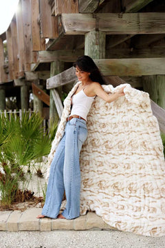 Woman draped in Hugs Marble Sand weighted blanket, showcasing its elegant tan marble print.