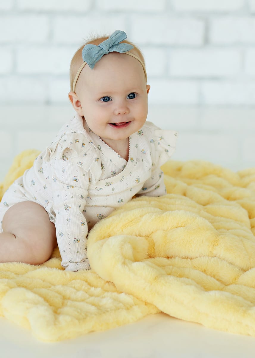 Baby smiling on a Hugs Butter Yellow Blanket, showcasing its plush texture and cheerful color.