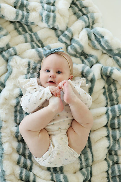 Baby enjoying the cozy Hugs French Stripe Blanket with playful blue stripes and soft cream background.