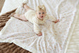 Baby lying on a Dainty Floral Blanket, featuring soft pink and blue flowers and plush cream backing.