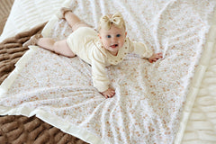 Baby lying on a Dainty Floral Blanket, featuring soft pink and blue flowers and plush cream backing.