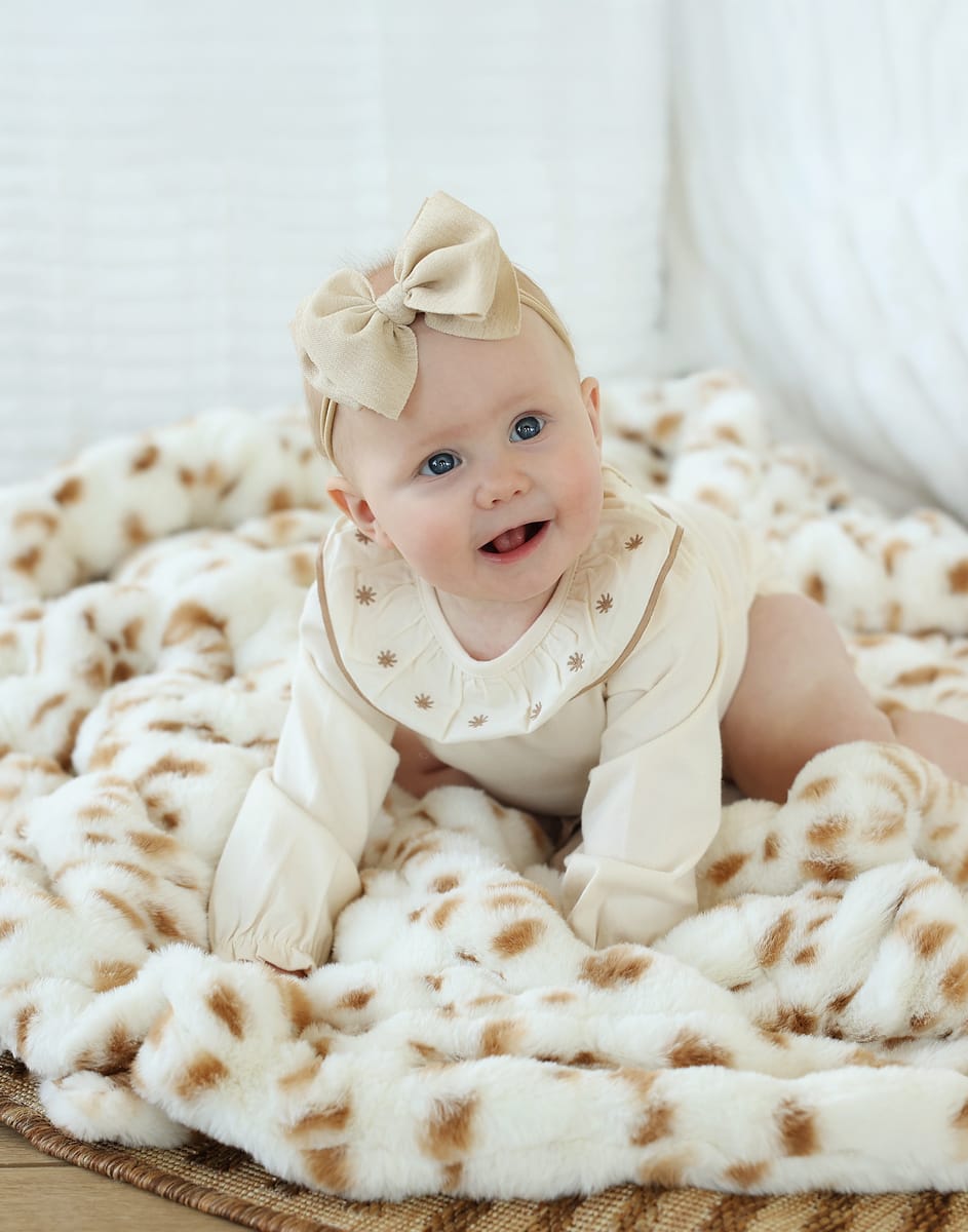 Baby smiling on a cozy Hugs Spotted Fawn Blanket with tan spots and cream background, showcasing comfort and style.