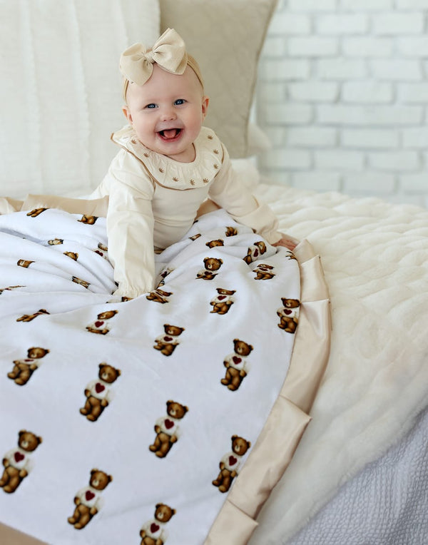 Baby smiling on Sweetheart Bear Blanket featuring cute teddy bears and a champagne satin ruffle.