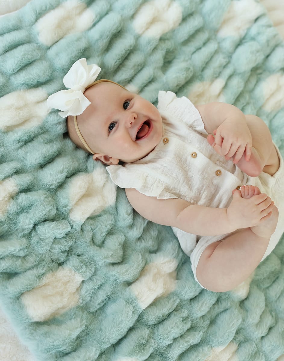 Baby smiling on a soft Hugs Polka Dot Tiffany Blanket, featuring cream polka dots on a Tiffany blue background.