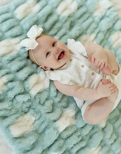 Baby smiling on a soft Hugs Polka Dot Tiffany Blanket, featuring cream polka dots on a Tiffany blue background.