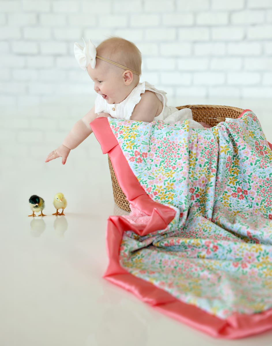 A baby playing with the Dainty Floral Pastel Blanket, featuring colorful flowers and a coral satin ruffle.
