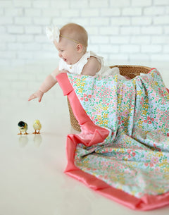 A baby playing with the Dainty Floral Pastel Blanket, featuring colorful flowers and a coral satin ruffle.