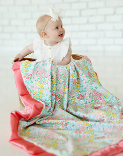 Dainty Floral Pastel Blanket draped over a baby in a basket, showcasing vibrant floral patterns and coral satin ruffle.