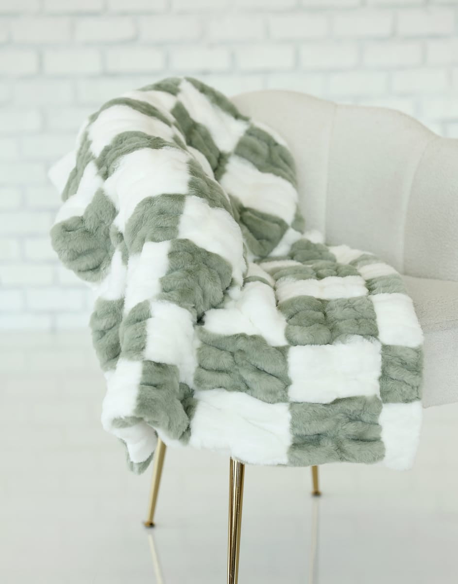 Hugs Check Sage Blanket draped over a chair, featuring a soft sage and white checkered pattern.