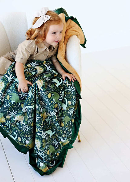 Little Dino Green Blanket wrapped around a child, showcasing playful dinosaur patterns on dark green background.