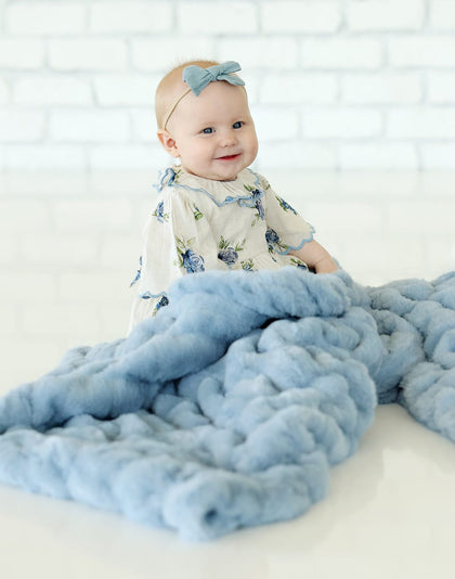 Baby smiling with Hugs Alaskan Blue Blanket, showcasing its plush texture and soothing blue color.