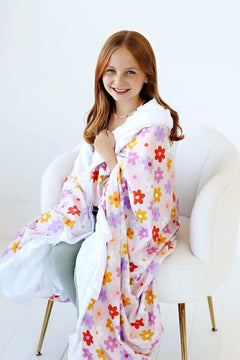 A girl wrapped in a vibrant Flower Power Blanket with floral design and white plush backing, smiling in a cozy setting.
