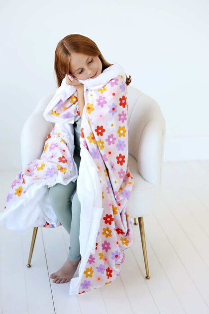 Child snuggling in the Flower Power Blanket featuring vibrant floral design and plush backing.