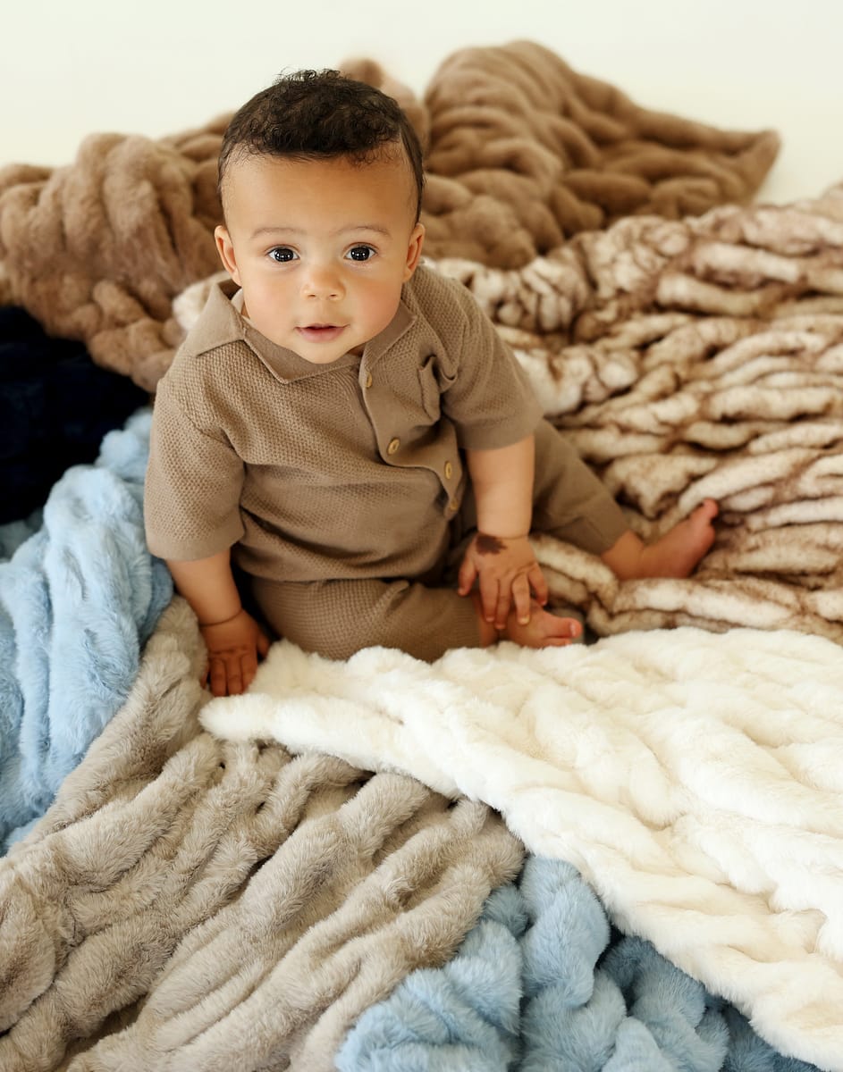 Baby sitting on a cozy arrangement of Hugs Topaz Blankets in various colors, showcasing their plush and elegant design.