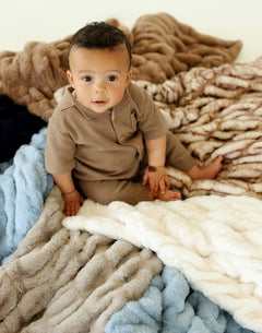Baby sitting on a cozy arrangement of Hugs Topaz Blankets in various colors, showcasing their plush and elegant design.