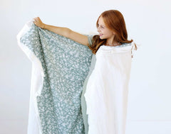 Girl showcasing the Dainty Floral Sage Blanket with floral pattern and cream satin ruffle in a cozy setting.