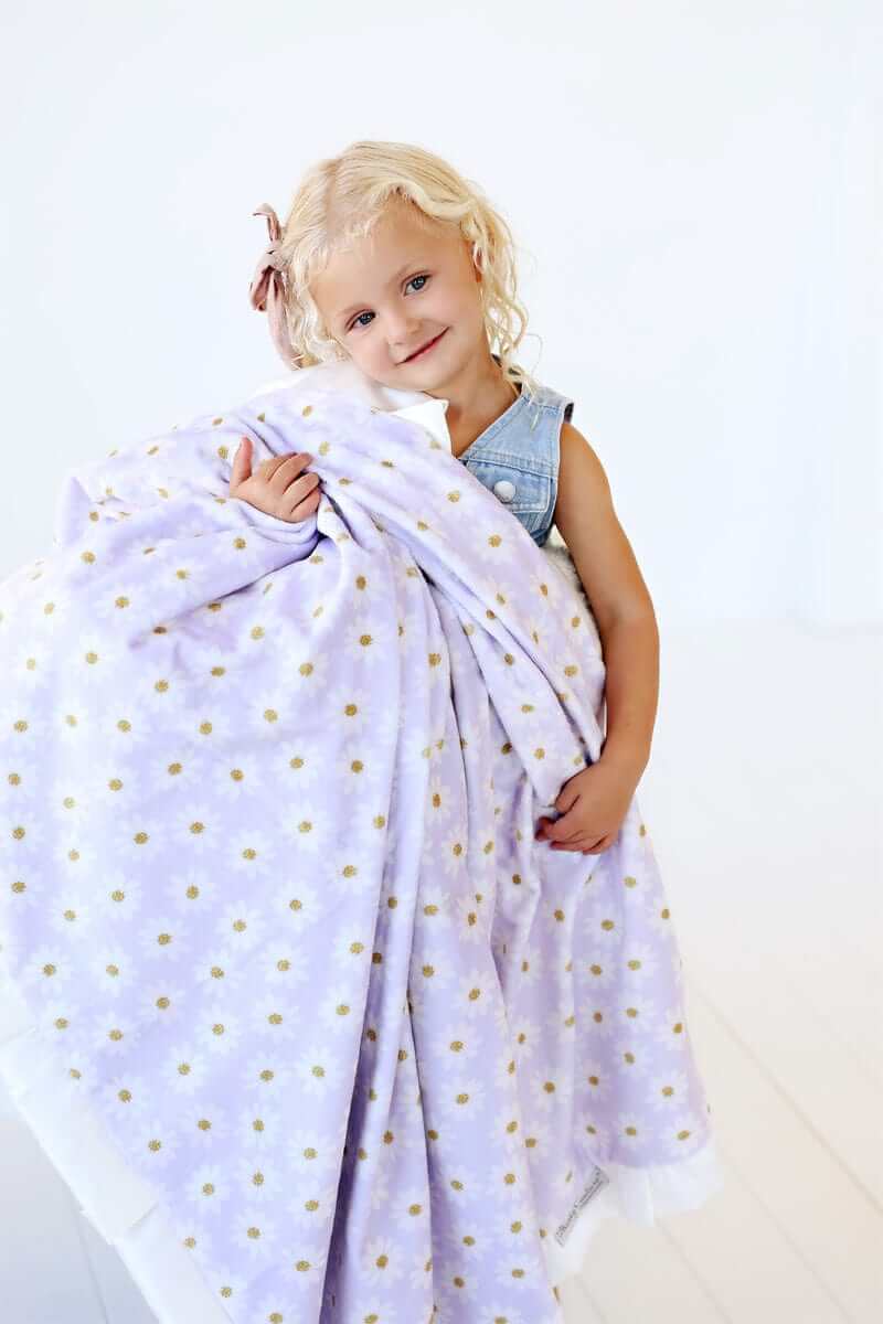 A child joyfully holding the Lavender Daisy Blanket featuring cheerful daisies on a lilac background.