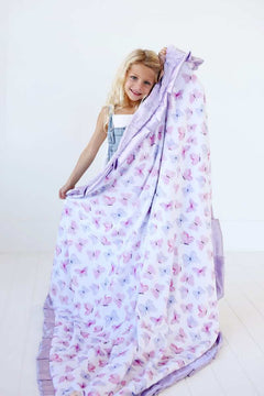 Girl smiling while holding a cozy Pastel Butterfly Blanket featuring pink and lilac butterflies on a soft white background.