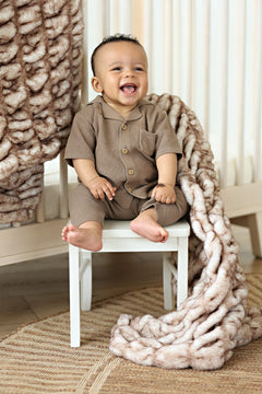 Happy baby wearing brown outfit sitting on a chair beside the cozy Hugs Topaz Blanket.