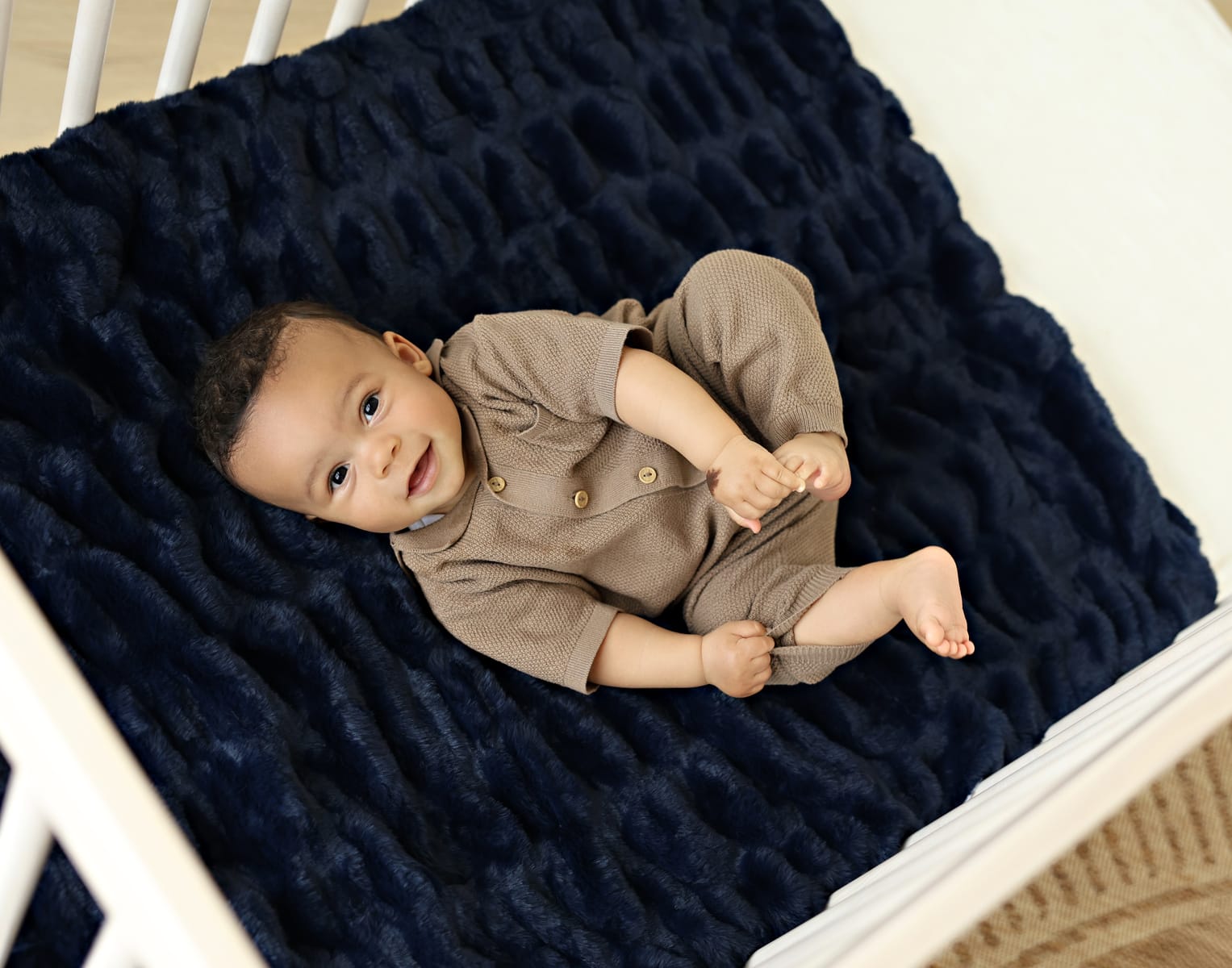 Infant lying on Hugs Navy Blanket in crib, showcasing its plush texture and classic navy blue color.