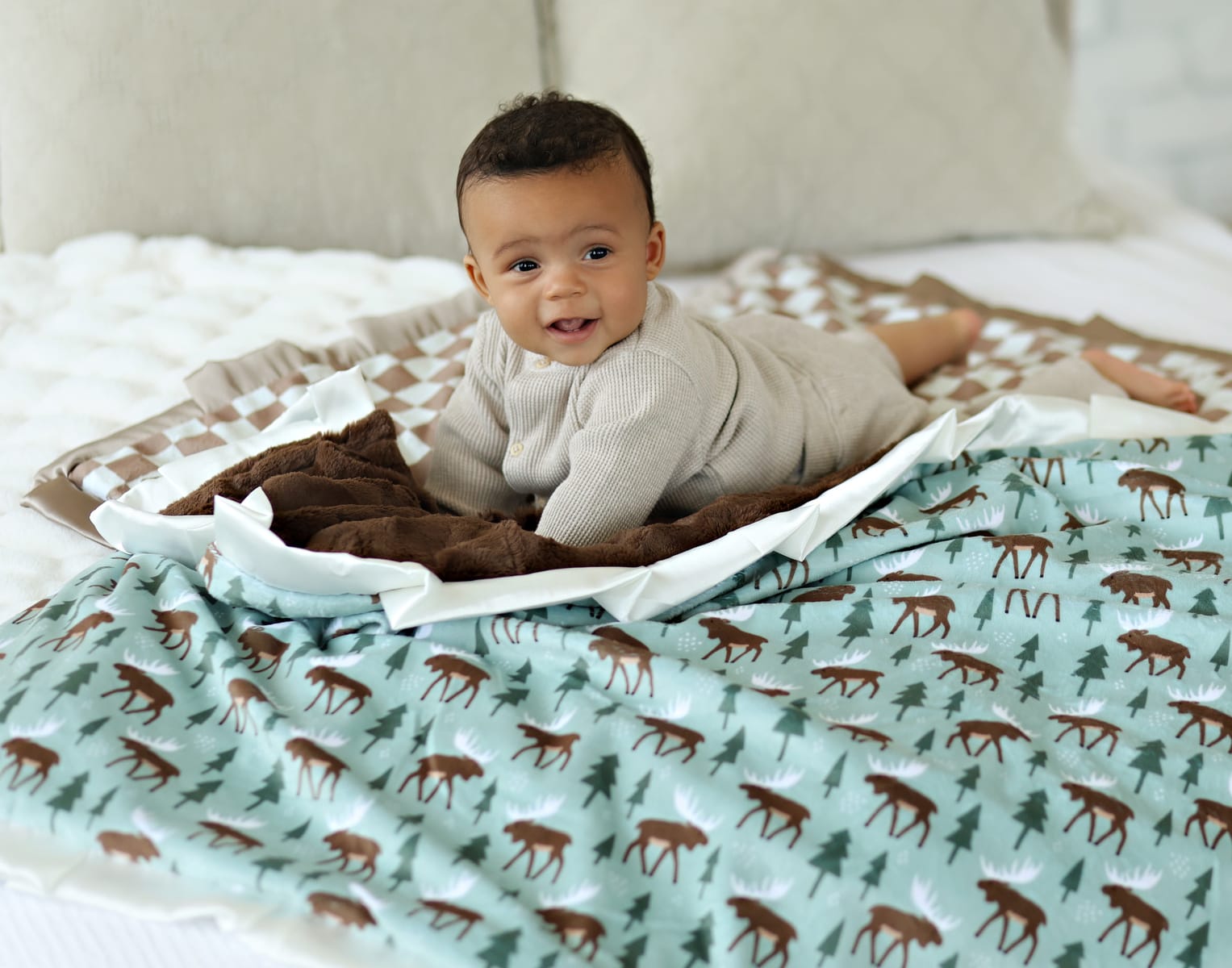 Happy baby on a Moose Blanket with charming moose and trees, showcasing a cozy woodland theme.