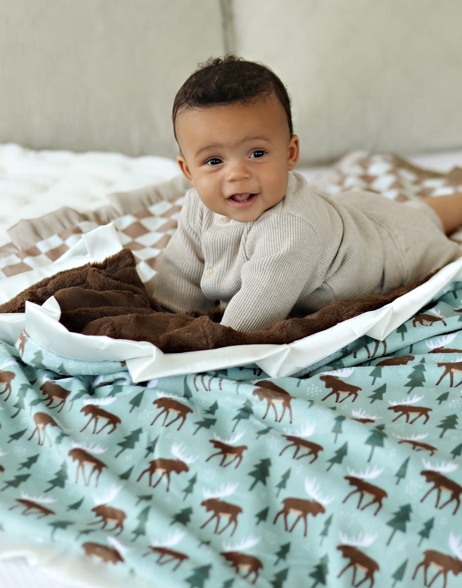 Baby lying on a cozy Moose Blanket featuring charming moose and trees, showcasing woodland vibes and plush textures.