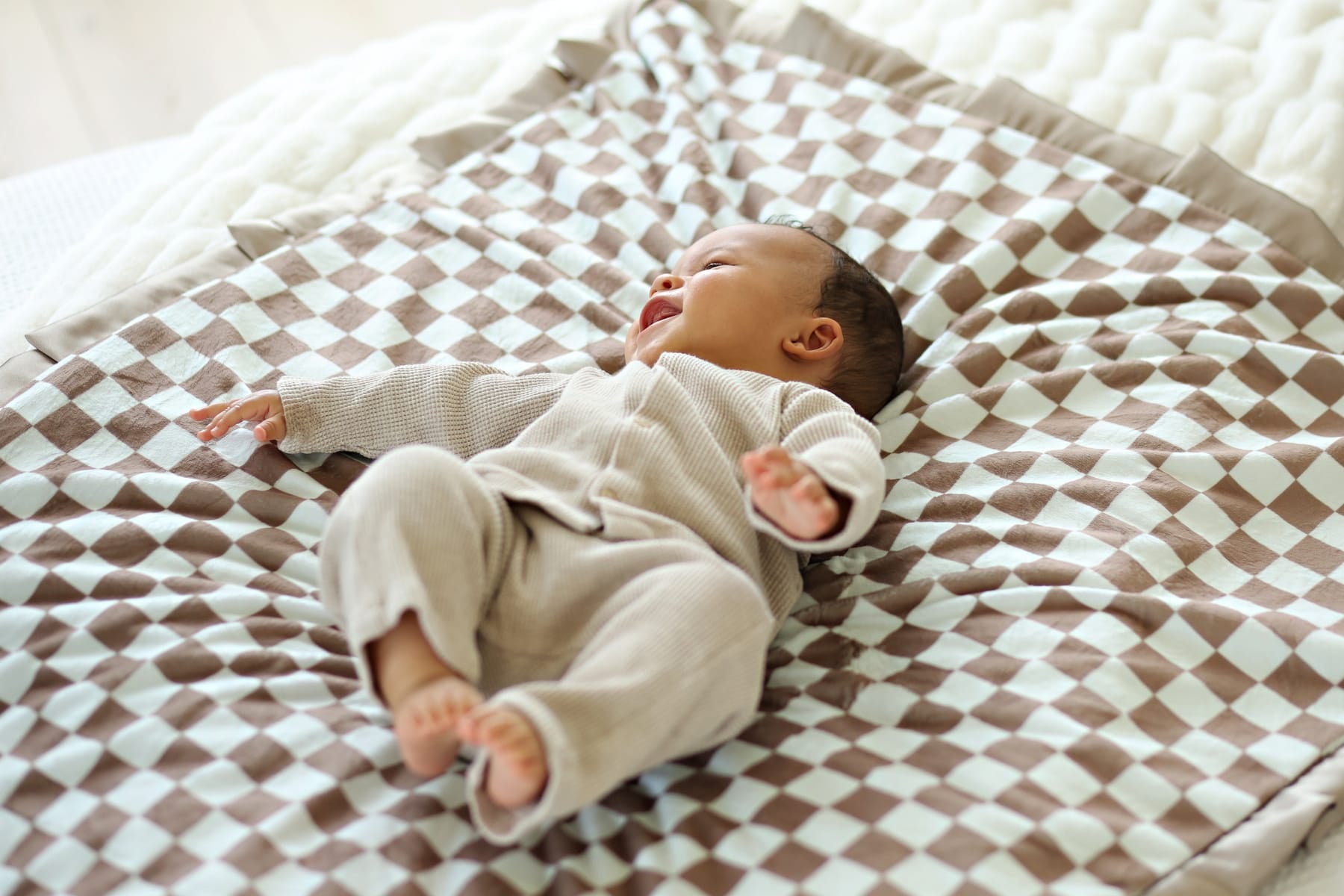 Baby joyfully lying on the Checkered Milk Chocolate Blanket featuring a light and dark yellow checkered pattern.