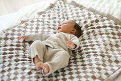 Baby joyfully lying on the Checkered Milk Chocolate Blanket featuring a light and dark yellow checkered pattern.