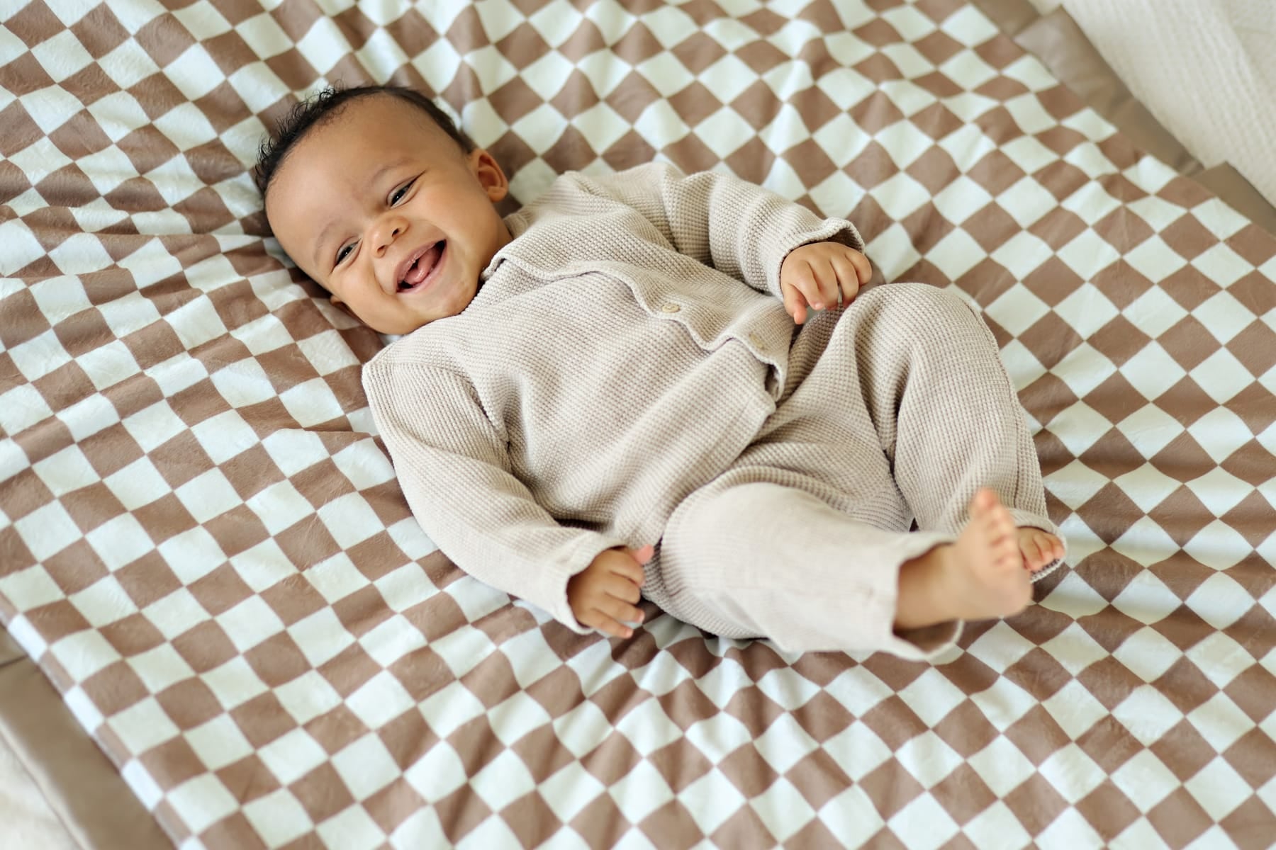 A happy baby lying on a Checkered Milk Chocolate Blanket with a light and dark checkered pattern.