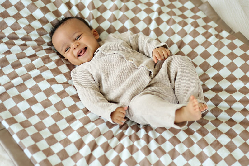 A happy baby lying on a Checkered Milk Chocolate Blanket with a light and dark checkered pattern.