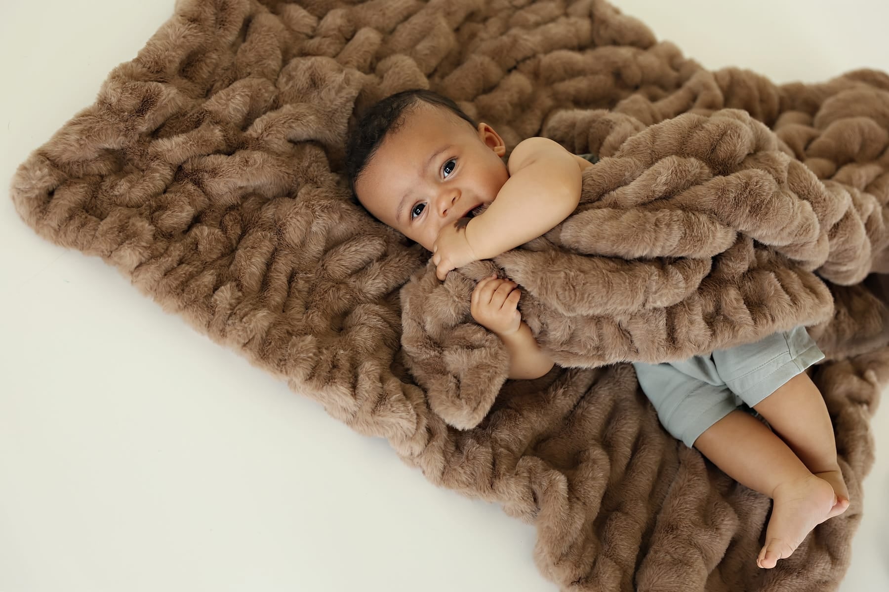 Baby snuggling with the Hugs Milk Chocolate Blanket, showcasing its cozy texture and rich brown hue.