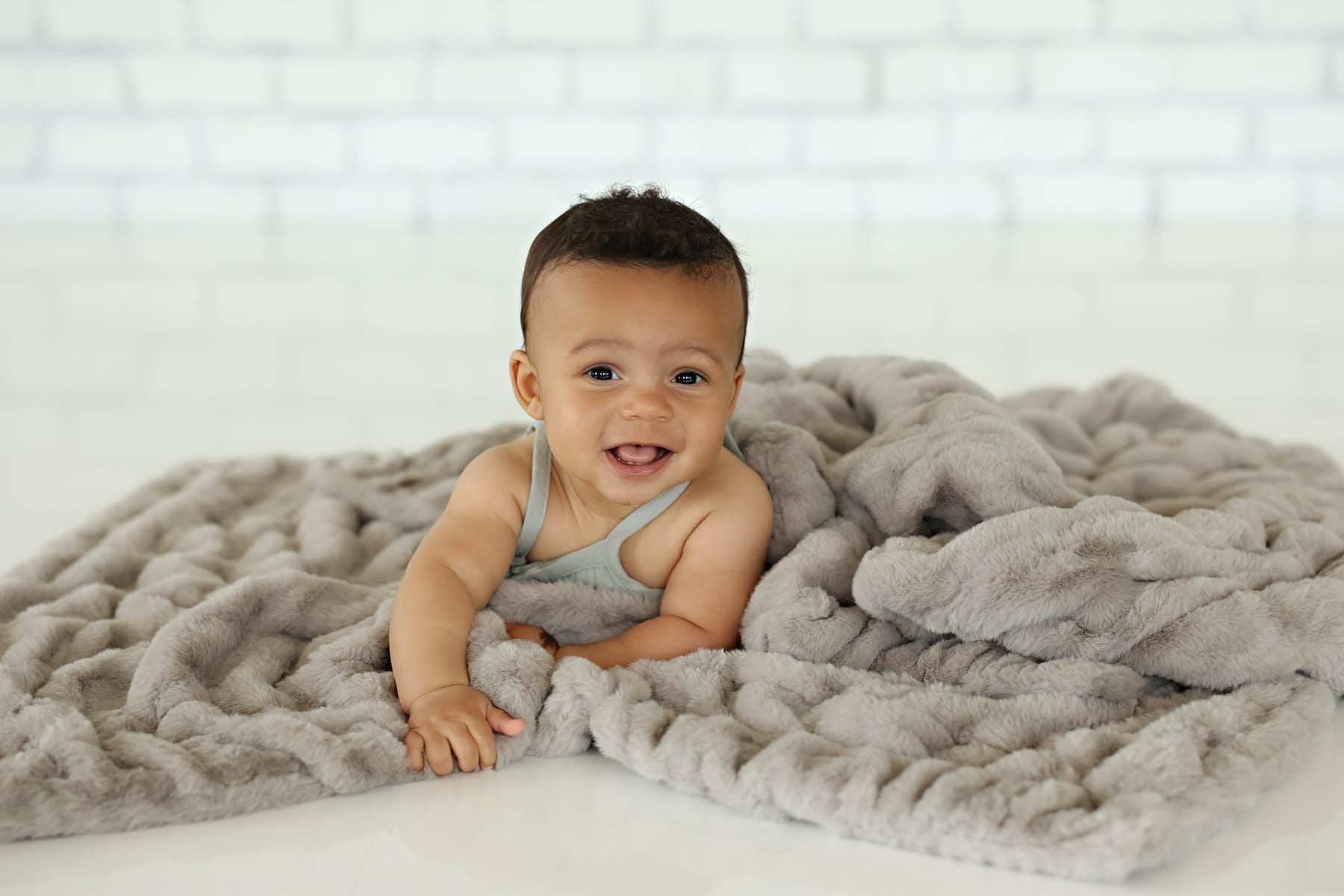 Happy baby wrapped in Hugs Tranquil Dove Blanket, showcasing its soft gray plush texture and comfort.
