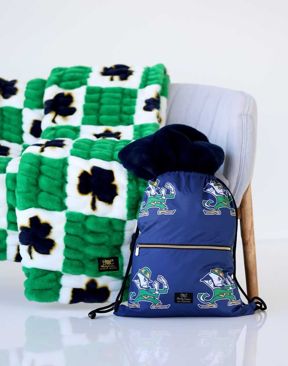 Minky Couture Notre Dame Fighting Irish Hooded Stadium Blanket next to a navy backpack on a chair.