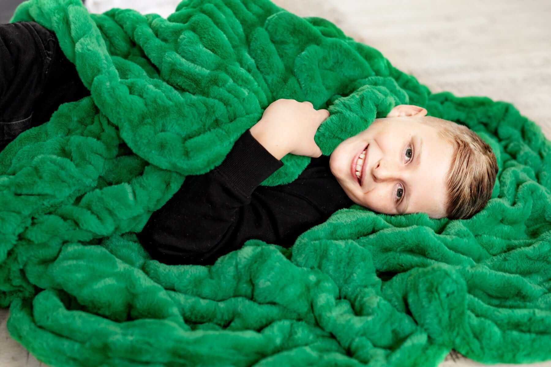 A child wrapped in the Hugs Green Blanket, showcasing its plush texture and vibrant green color.