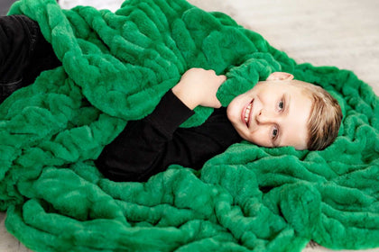 A child wrapped in the Hugs Green Blanket, showcasing its plush texture and vibrant green color.