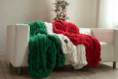 Hugs Blankets draped over a white couch, showcasing its plush green, red, and white fabric in a cozy setting.