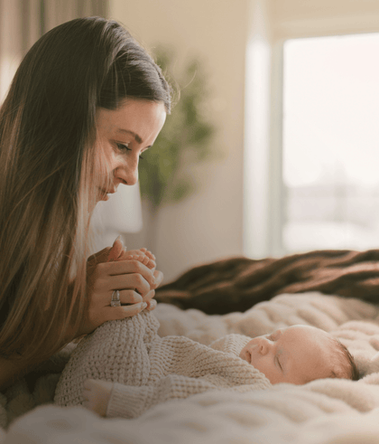 A mother gently holding her baby's feet, smiling affectionately. Soft lighting creates a warm, tender atmosphere.