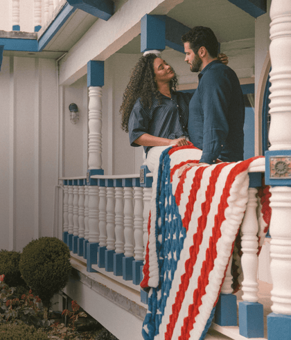 Couple embracing on a balcony with patriotic decorations, showcasing an elegant coastal home setting.