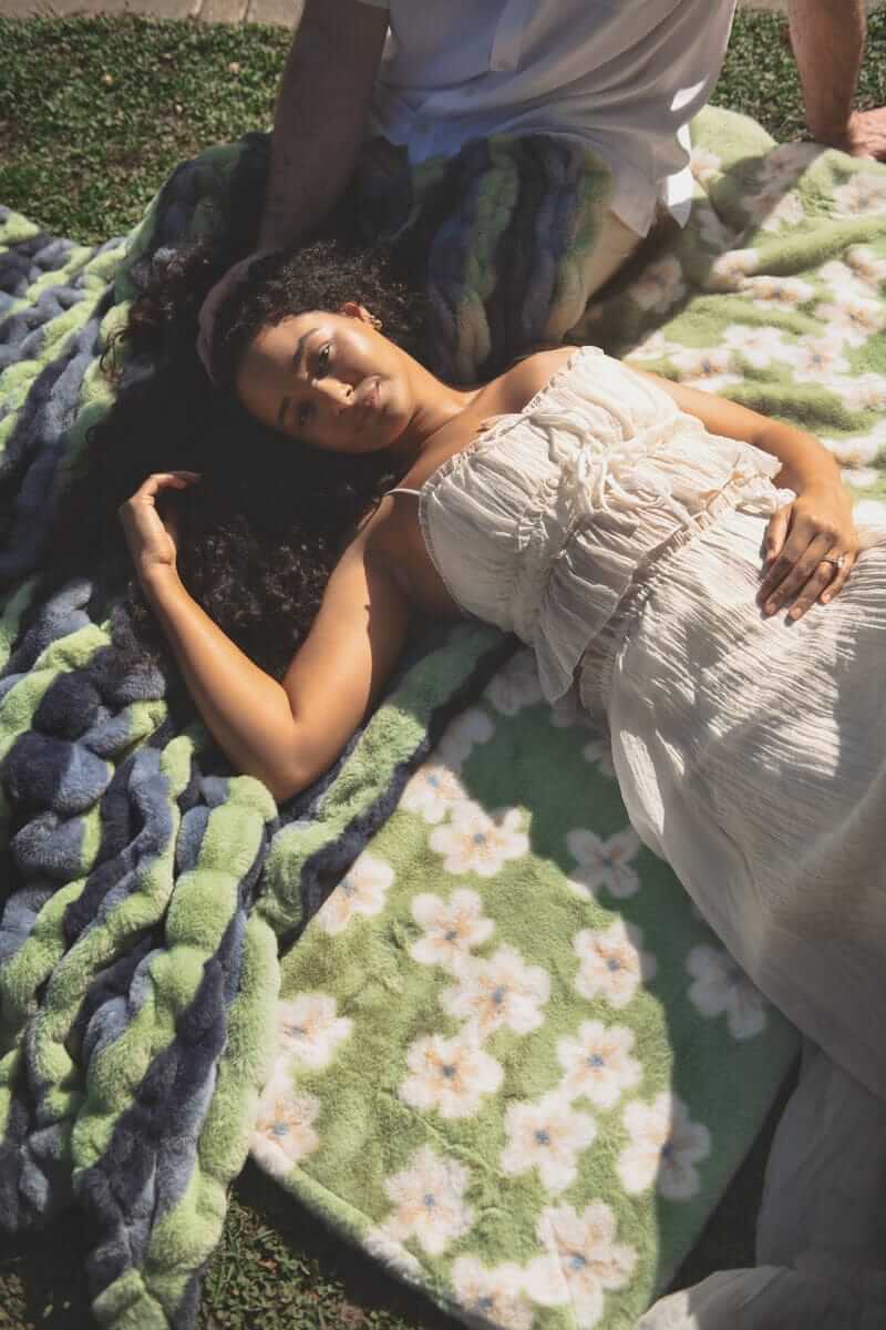 Model relaxing on the Lush Mist Floral Blanket featuring a floral design and plush texture.
