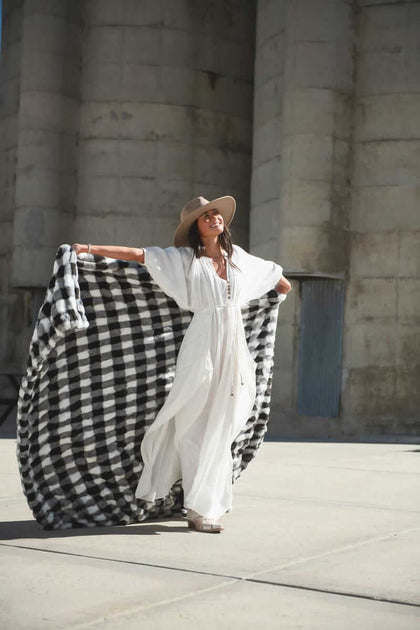 Woman in a white dress holding the Hugs Gingham Charcoal Blanket outdoors, showcasing its stylish design.